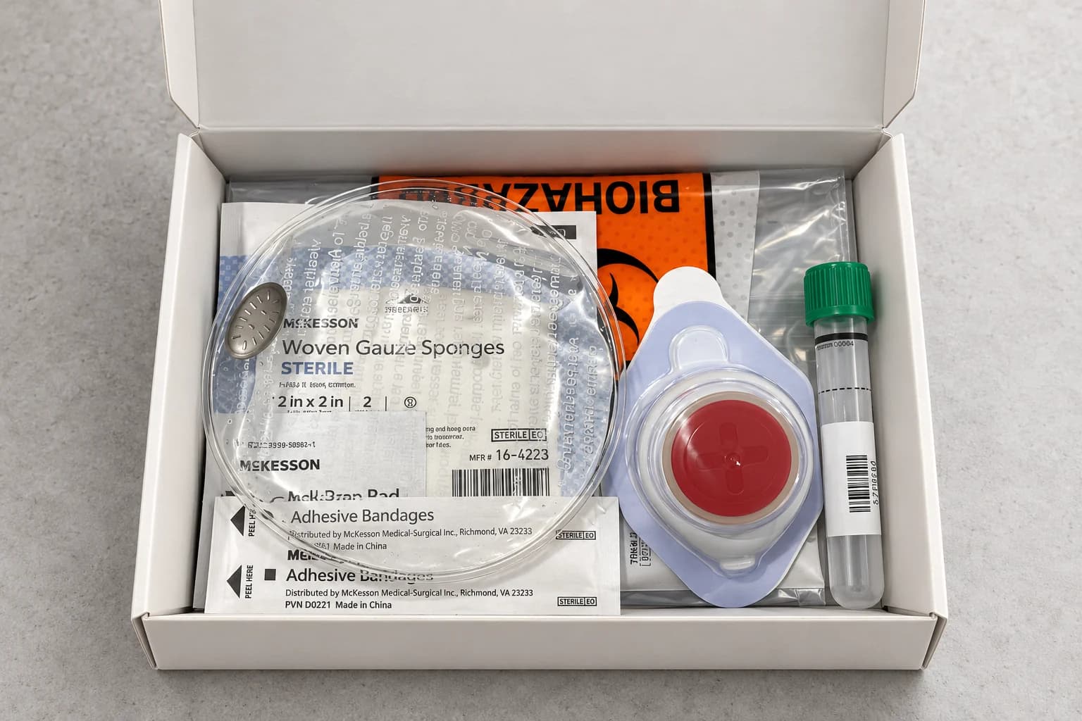 The kit open, seen from above, with packets of gauze and bandages and a clear round warming pack on the left, the round collection device and a green-capped tube on the right, and an orange biohazard bag at the back.